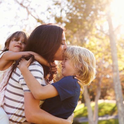 Mother Carrying Son And Daughter As They Play In Park